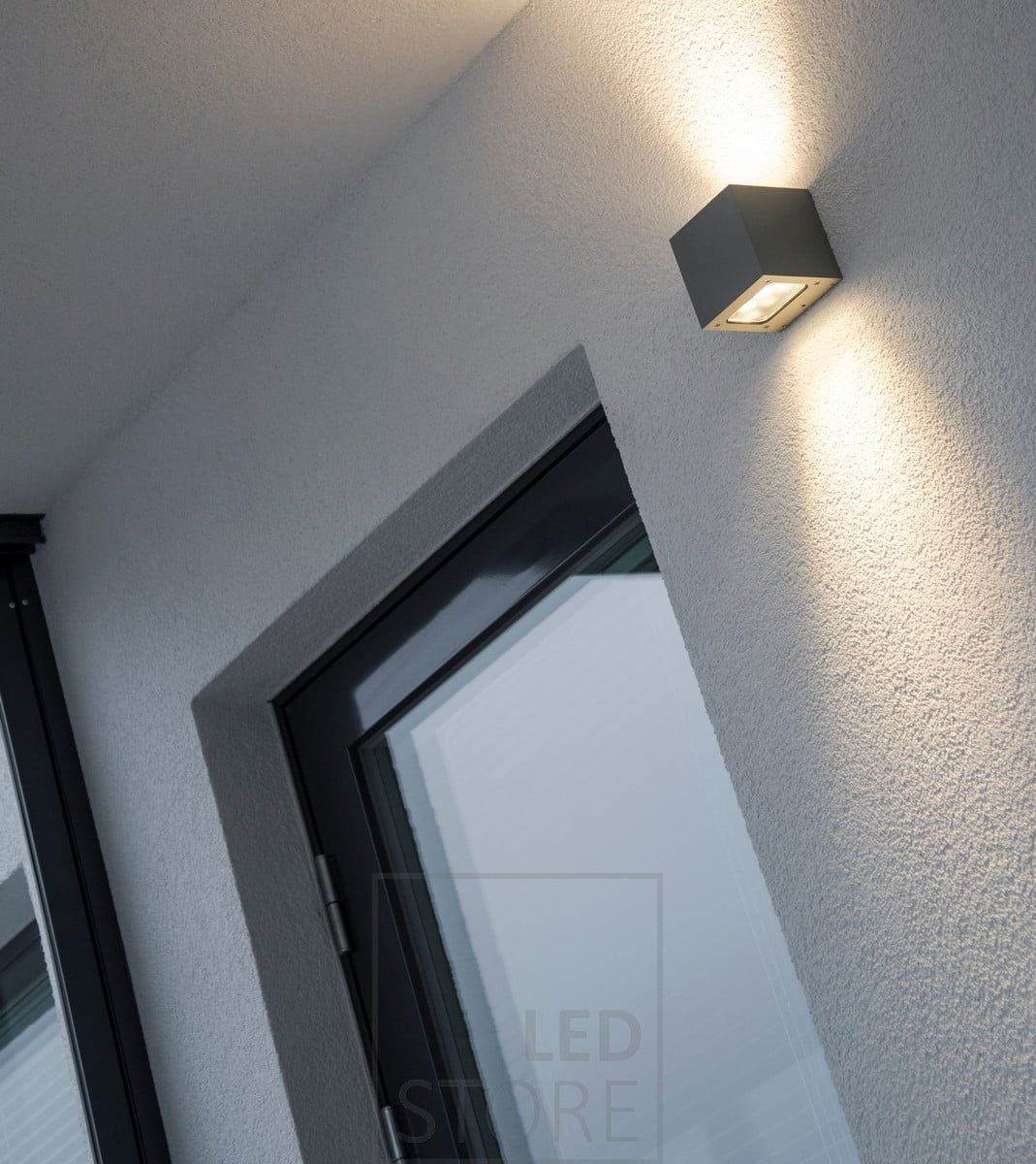 A bi-directional LED wall light on the facade of a house. The luminaire provides atmospheric light through the wall, and indirect light through the covered terrace. Ledstore.fi